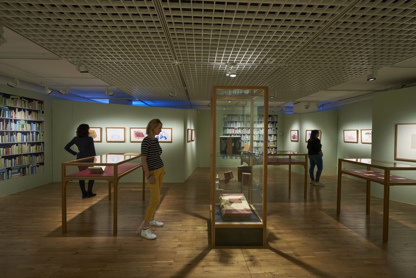 Im Raum einer Ausstellung schauen sie drei Menschen Objekte an.